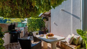 An outdoor patio with a table, chairs, a grill, and potted plants.
