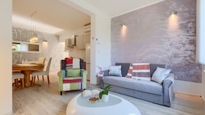 Un salon moderne comprenant un canapé, un fauteuil coloré, un coin repas avec une table en bois et un grand tableau abstrait accroché au mur.