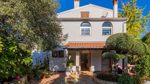 A two-story house with a tiled roof, a front entrance, and a small garden with potted plants.