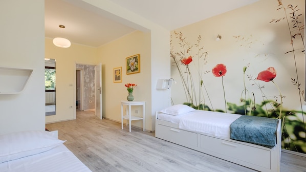 A bedroom with a bed, a bedside table, a wall-mounted lamp, and a window.