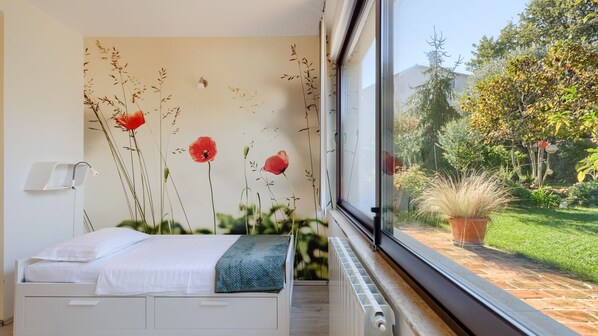 Ein Schlafzimmer mit Bett, einer Wandleuchte und einem Fenster mit Blick auf einen Garten.