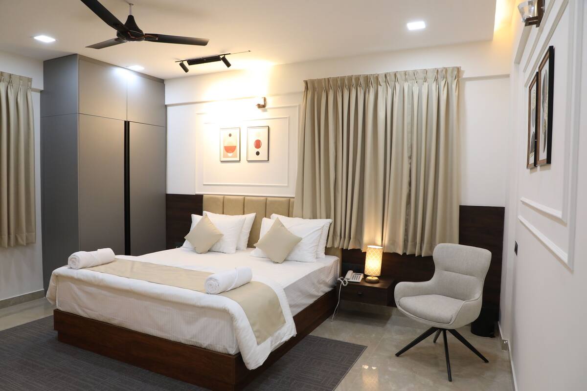 A modern hotel room with a large bed, a bedside table with a lamp, a chair, and a ceiling fan.