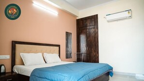 A bedroom with a bed, a wardrobe, a wall-mounted air conditioner, and a wall decoration. - Ranthambore Hotel and Restaurant (Jaipur)