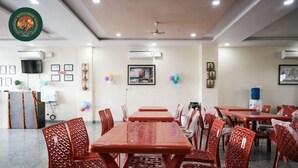 A dining area with red tables and chairs, air conditioning units, framed pictures on the walls, and a ceiling fan. - Ranthambore Hotel and Restaurant (Jaipur)