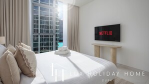 A modern hotel room with a large bed, a flat-screen TV, and a view of a building and pool. - LUX The Burj Khalifa Lagoon View Suite 4 (Dubai)