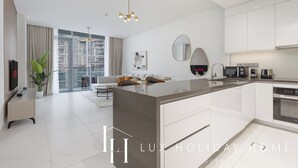 A modern, well-lit living area with a kitchen, large windows, and a view of the city. - LUX The Burj Khalifa Lagoon View Suite 4 (Dubai)
