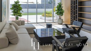 A modern living room with a sofa, coffee table, and chairs, large windows, and indoor plants. - LUX The Burj Khalifa Lagoon View Suite 4 (Dubai)