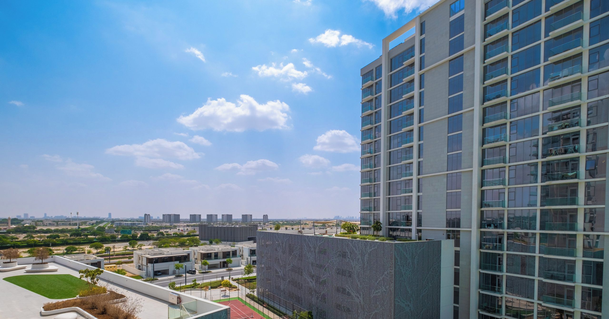 A modern building with a rooftop sports area, including a tennis court and landscaped gardens.