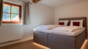 A bedroom with a bed, a window, and a wooden ceiling beam.