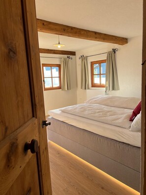 Ein Schlafzimmer mit Holzboden, einem Bett mit weißer Bettwäsche und zwei Fenstern mit Vorhängen.