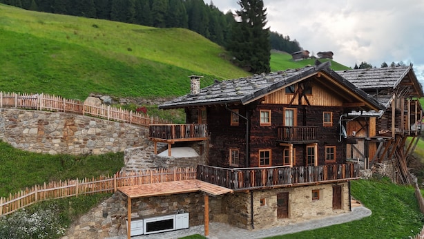 A wooden chalet with a stone staircase, wooden deck, and a stone wall.
