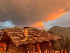 Eine rustikale Holzhütte mit einem Steinkamin, umgeben von Bergen und einem Abendhimmel.