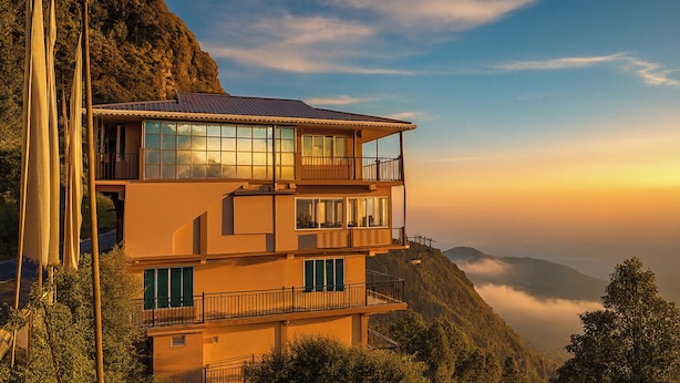 Un edificio de varios pisos con grandes ventanales, balcones y montañas al fondo.