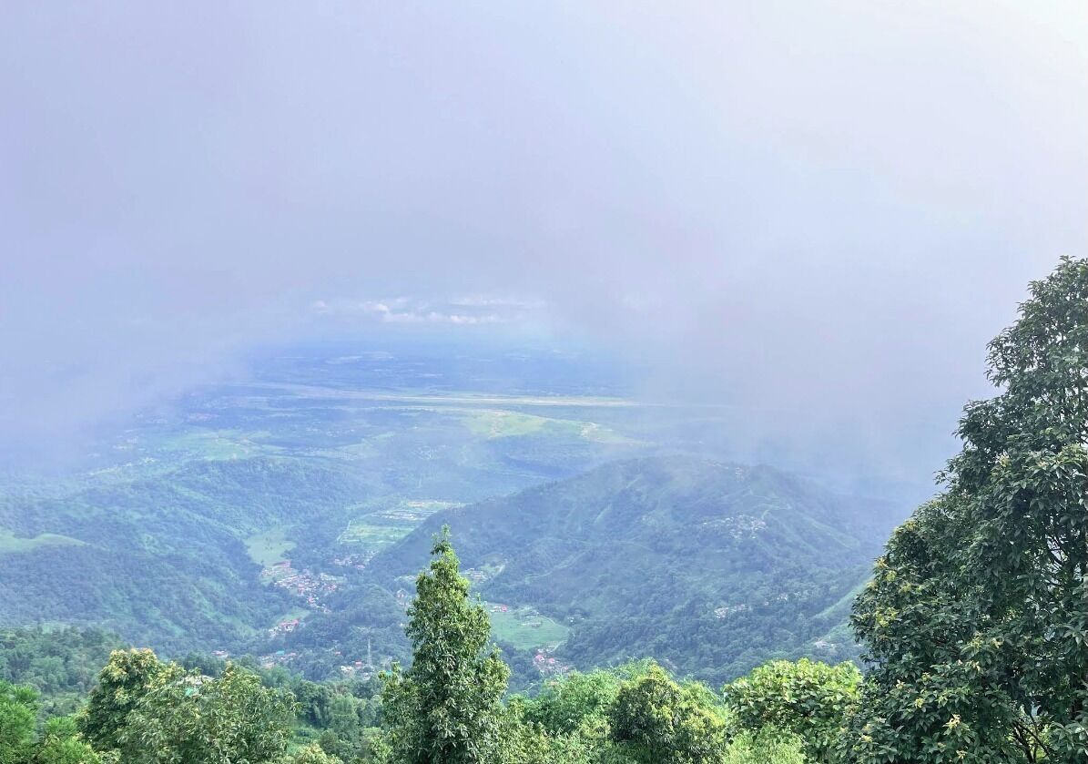 A panoramic view of a mountainous landscape with dense greenery and a valley below.
