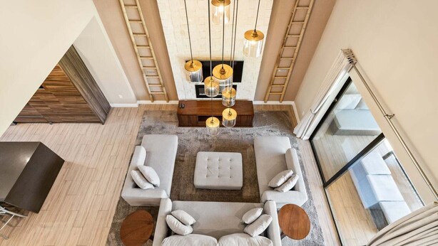 Un salon moderne avec un ensemble de canapés, une table basse et un téléviseur. Le sol est en bois, il y a une cheminée et une vue sur l’extérieur.