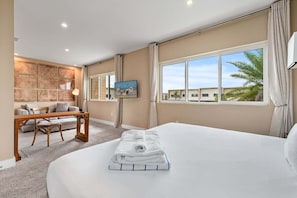 A hotel room with a bed, a desk, a chair, a TV, and a window with a view of palm trees.