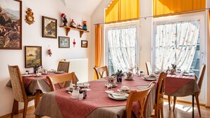 Comedor con una mesa preparada para cuatro personas, rodeada de sillas, obras de arte en las paredes y una ventana con cortinas.