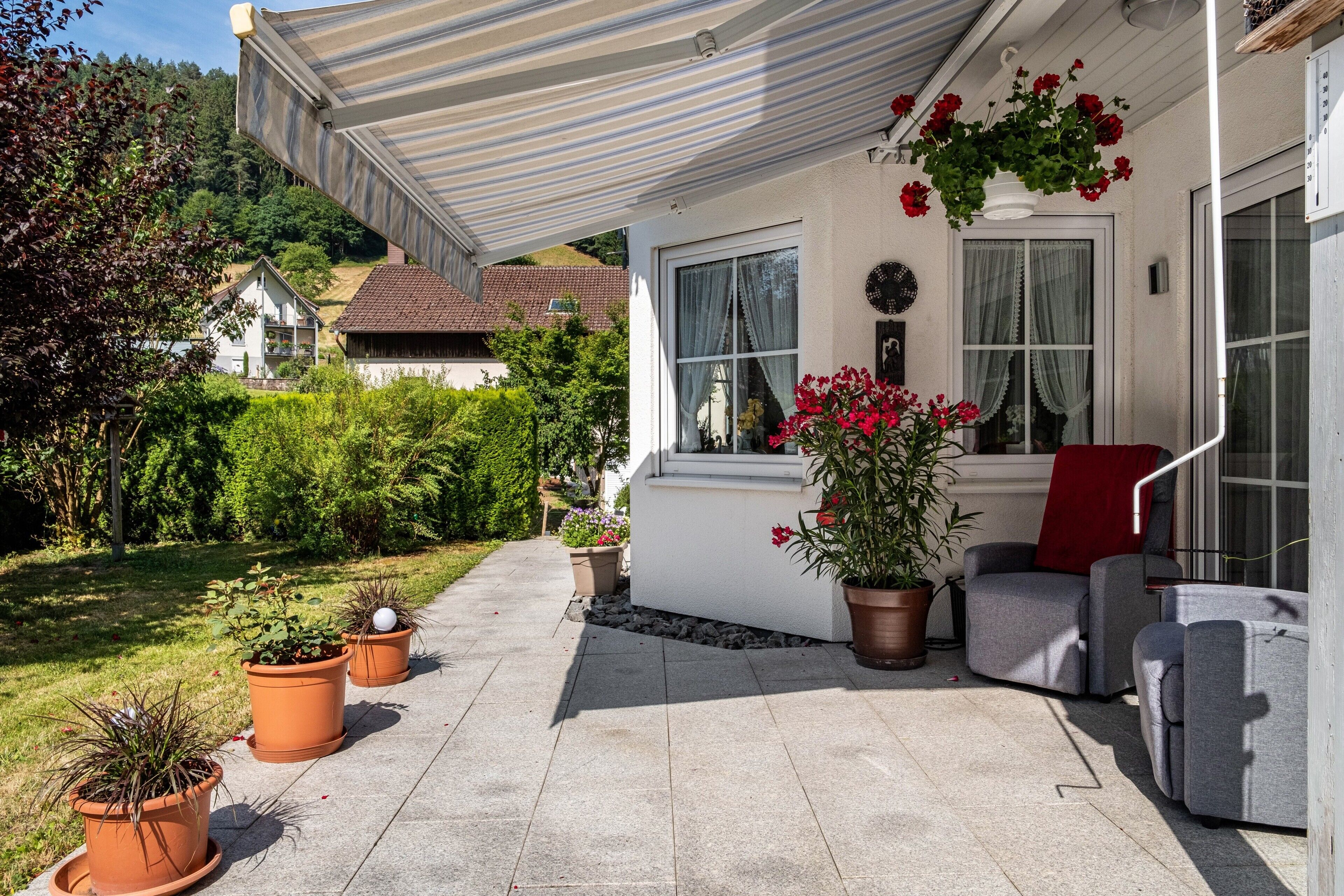 A covered patio area with outdoor furniture, potted plants, and a view of a hillside.