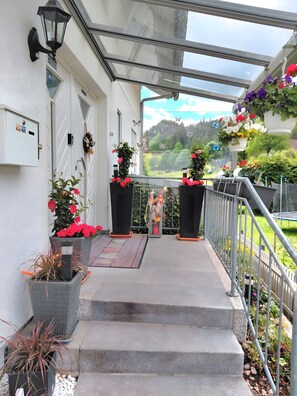 Un espace extérieur abrité, avec des marches menant à une porte, des plantes en pot et une vue sur un paysage verdoyant.