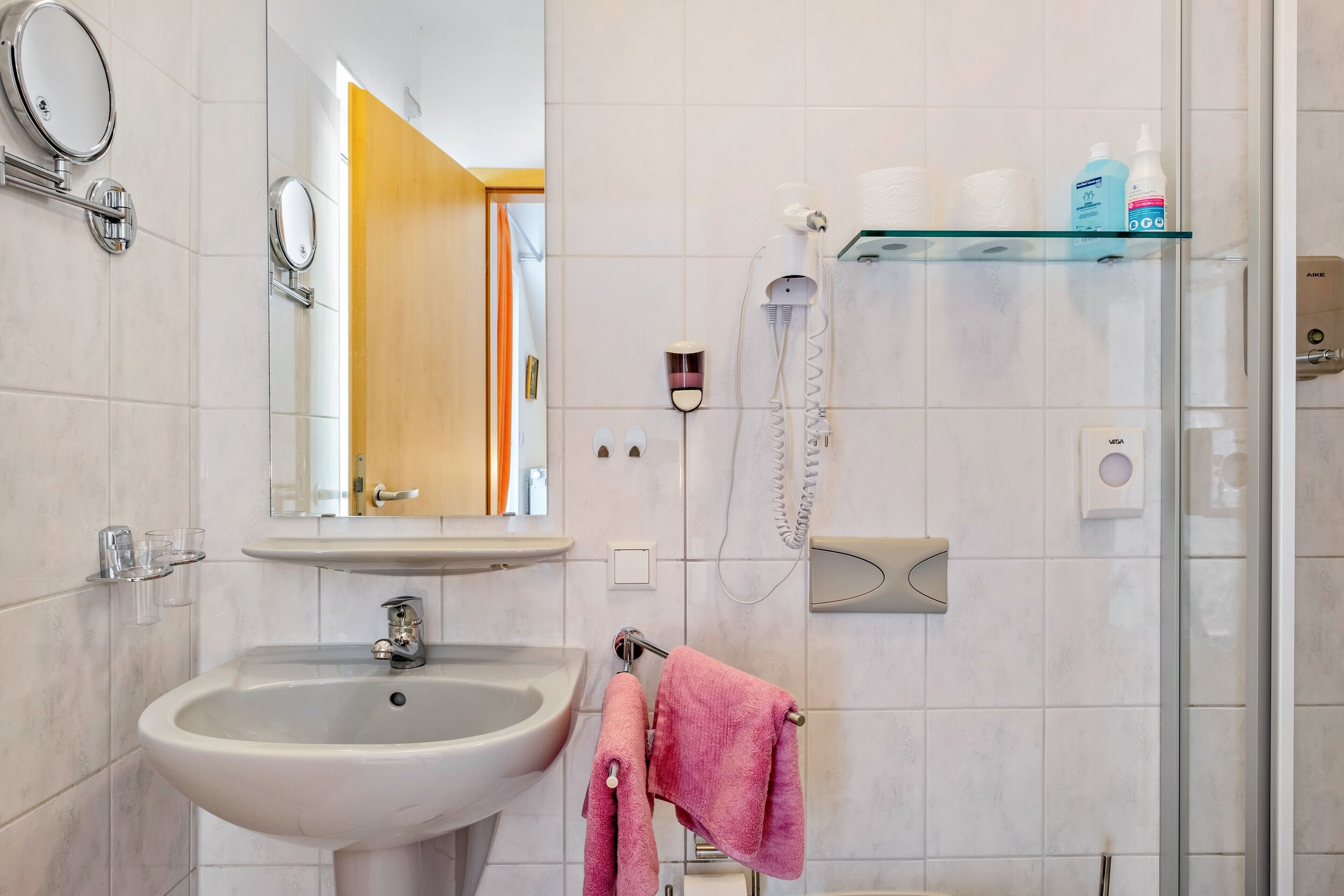Une salle de bain équipée d’un lavabo, d’un miroir, d’un porte-serviettes et d’une cabine de douche en verre.