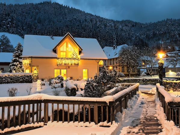 Un bâtiment enneigé doté d’un balcon, entouré d’arbres chargés de neige et d’une clôture en bois.