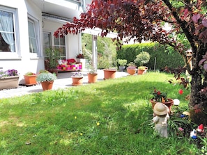 Un jardin bien entretenu, agrémenté de diverses plantes en pot, d’un gnome décoratif et d’un espace patio avec un canapé et des coussins.
