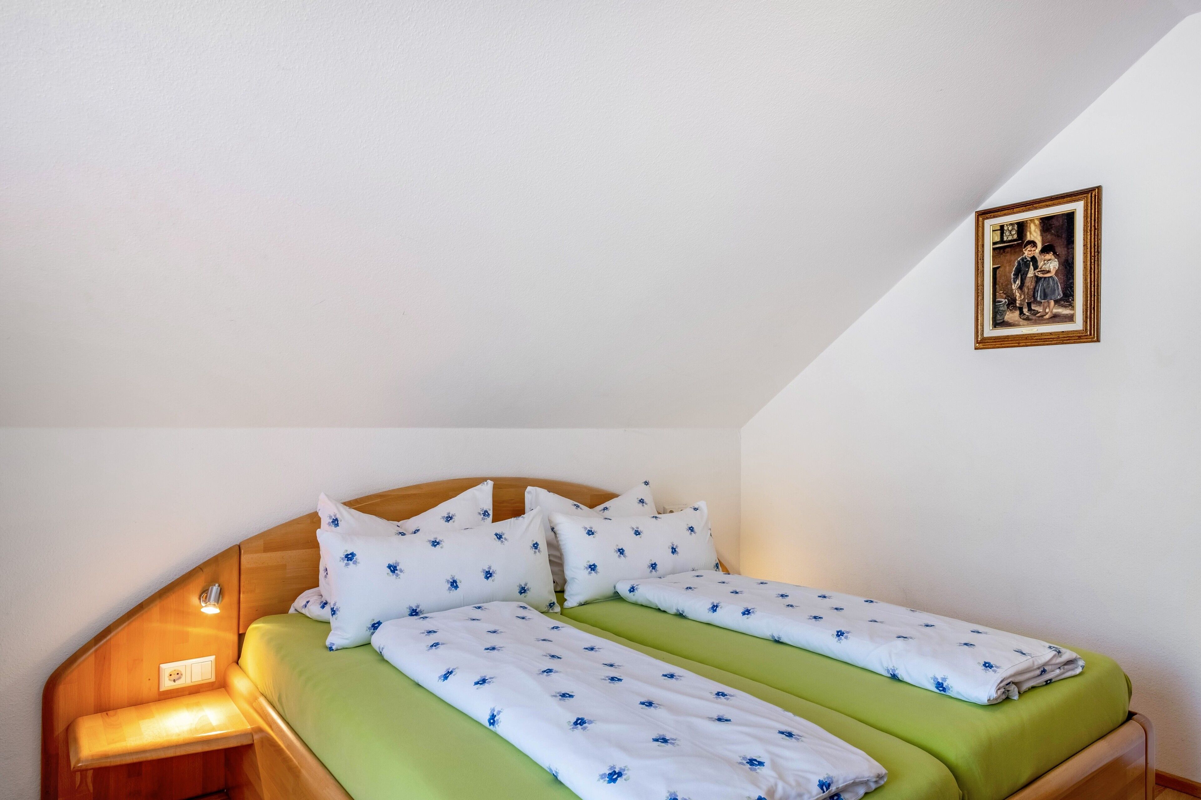 Une pièce comprenant un lit, une table de chevet, un tableau accroché au mur et un plafond en pente.