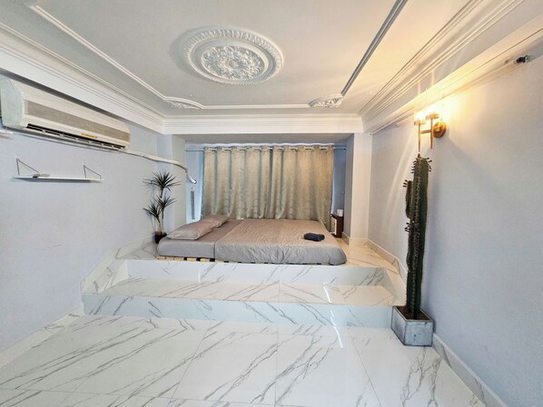 Quarto com cama, planta em vaso, mesa de cabeceira e ar-condicionado fixado na parede.