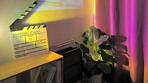 A clapperboard with 'Universal Studios' and 'Scene 11' written on it, a camera on a tripod, a plant, and a bookshelf with a calendar showing '1 APR'. - H2T Hotel - Center Bui Vien (Ho Chi Minh City)
