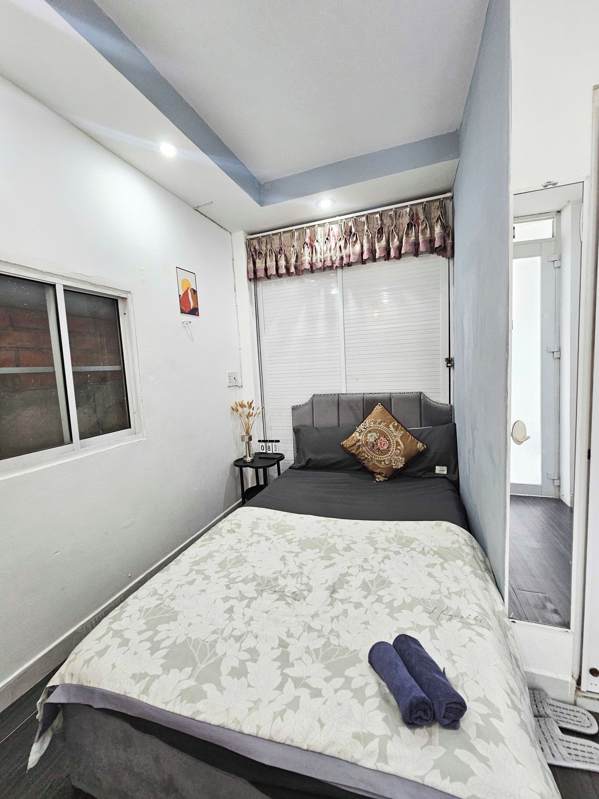 A bedroom with a bed, a window, a bedside table, and a door.