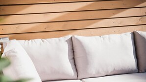 A wooden bench with cushions, a wooden table, and greenery in the foreground. - Fjell Apart Schladming-Dachstein (Gröbming)