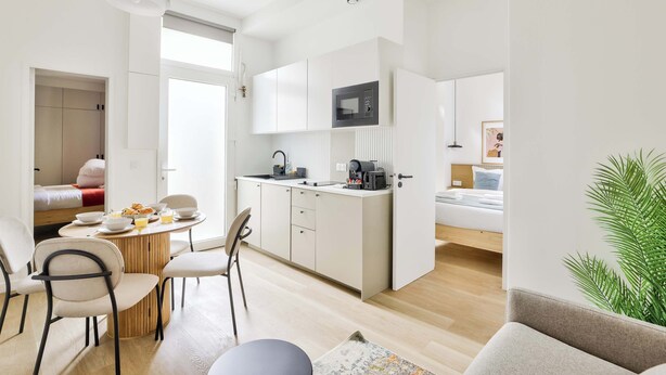 Une cuisine moderne avec des meubles blancs, un four à micro-ondes et une machine à café. On y trouve également un coin repas avec une table ronde et des chaises.