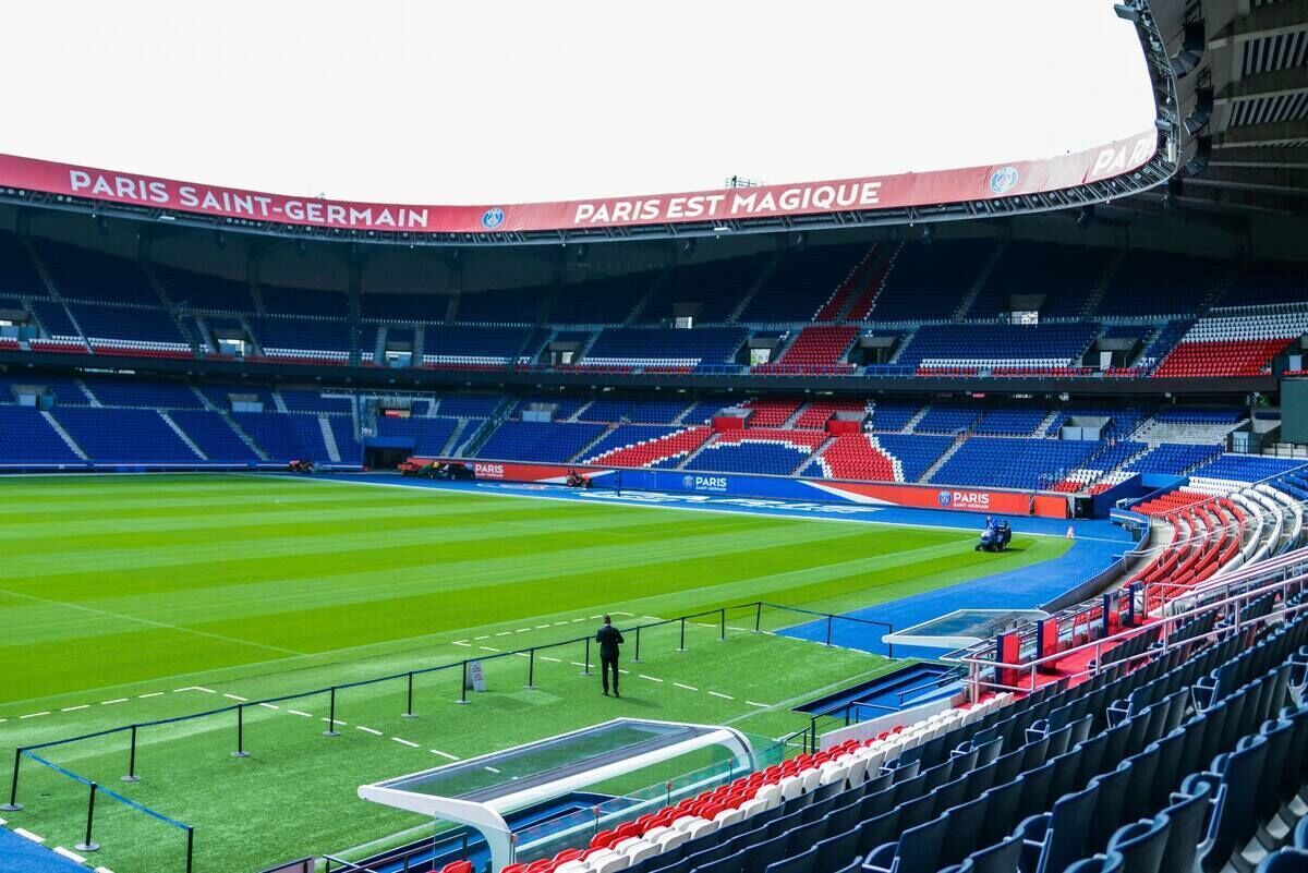 Un stade avec des gradins vides, un terrain verdoyant et un toit orné d’enseignes.
