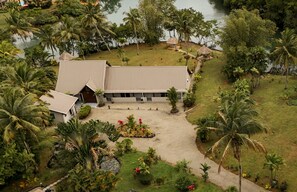 An aerial view of a resort with a large building, palm trees, and a water body.