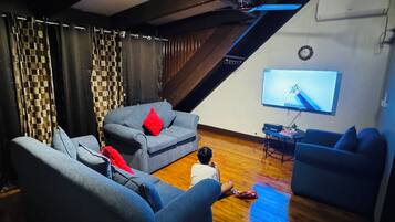 Una habitación con techo inclinado, vigas de madera, un televisor de pantalla plana montado en la pared y suelo de madera.