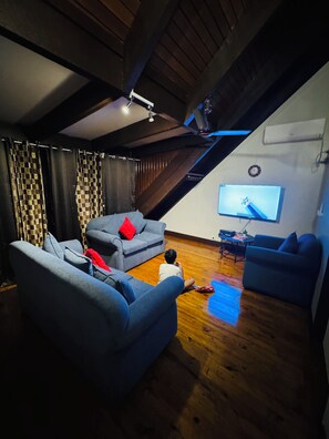 A room with a sloped ceiling, wooden beams, a flat-screen TV mounted on the wall, and a wooden floor.