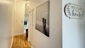A hallway with a wooden floor, a welcome sign, and a framed picture on the wall.