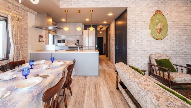 Una cocina moderna con una isla central, mesa de comedor con vajilla azul y un sofá estampado en una habitación con paredes de ladrillo visto.