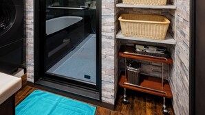 Un baño con puerta de cristal, suelo de madera, una toalla azul y cestos de mimbre en estantes.