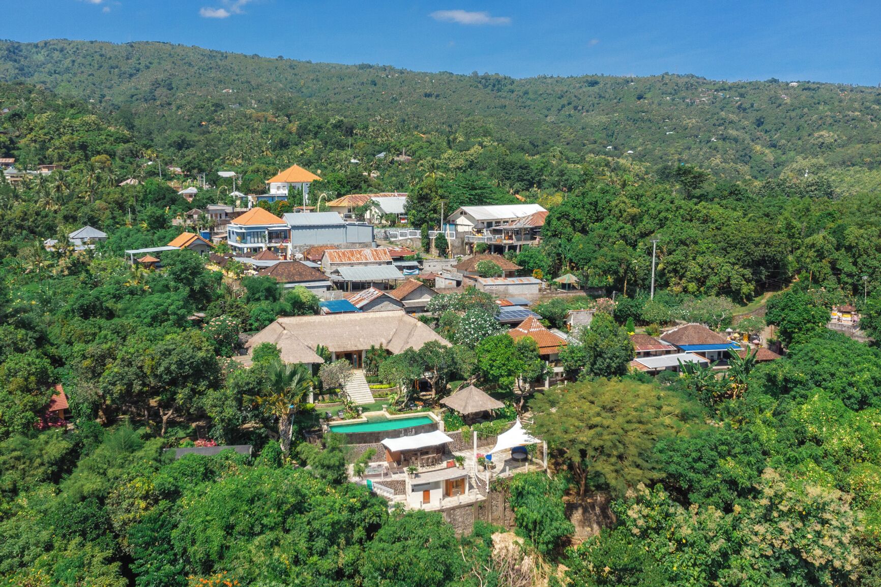 Un pueblo en una ladera con edificios tradicionales y modernos, rodeado de vegetación exuberante y colinas.
