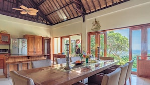 A spacious dining area with a long wooden table, surrounded by chairs, and a view of lush greenery outside. - Bougainville Hill Villa (Sukasada)