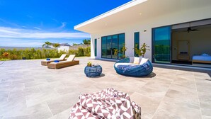 Eine moderne Terrassengestaltung mit Liegestühlen, einem Sitzsack mit Muster und einem vom Glas umschlossenen Schlafzimmer.