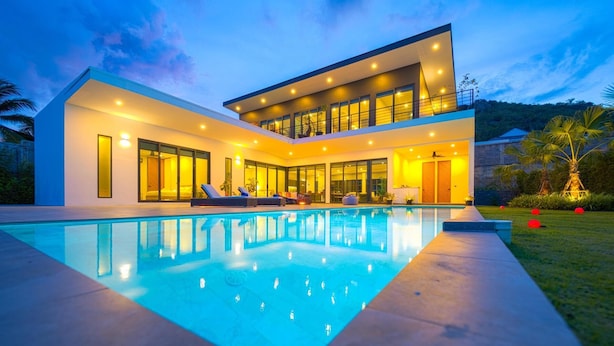 Ein modernes, zweistöckiges Haus mit Pool, großen Fenstern und Sitzgelegenheiten im Freien.