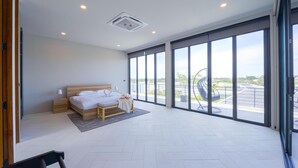 Ein modernes Hotelzimmer mit einem großen Bett, einem kleinen Nachttisch, einem Sessel und Blick auf die Stadt durch raumhohe Fenster.