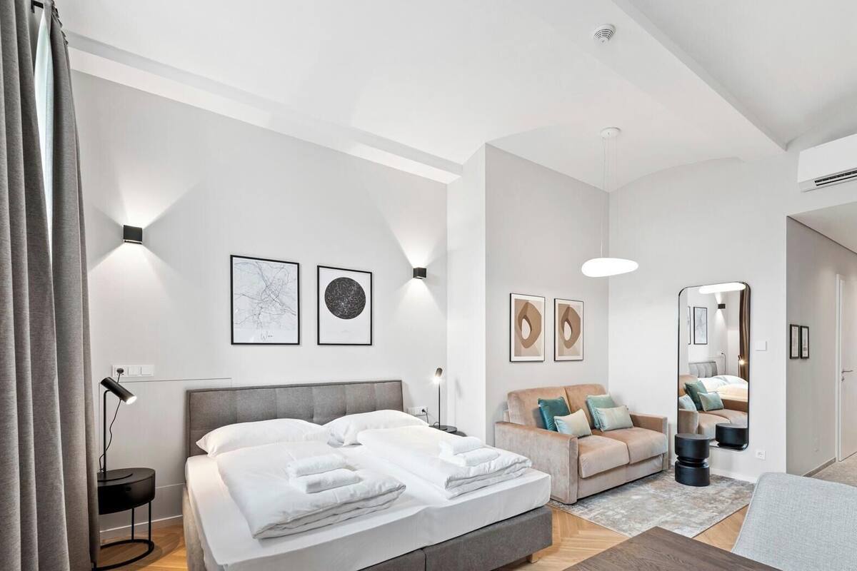 A modern bedroom with a bed, bedside tables, a sofa, a mirror, and artwork on the walls.