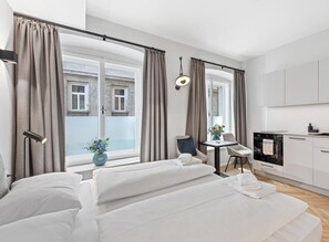 A modern bedroom with a large bed, a small desk, and a kitchenette. - easy-flat Stadtpark - Premium AC Apartments (Vienna)