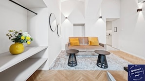 Een modern appartement met een zithoek, twee bijzettafels en een gele vaas met bloemen.