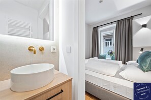 Un baño moderno con un lavamanos grande de color blanco, grifos dorados y un mueble de tocador de madera.