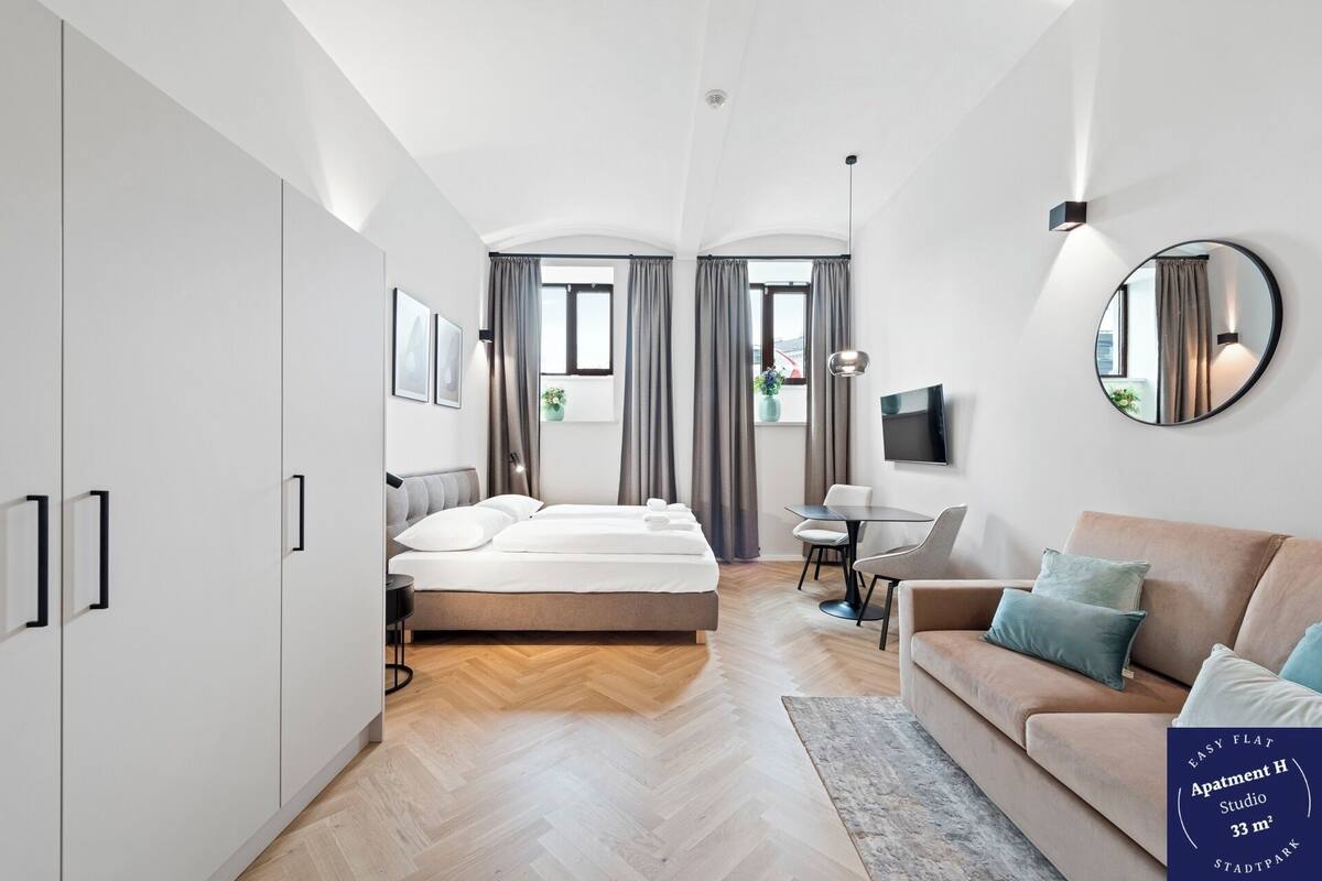 A modern hotel room with a bed, a sofa, a desk, and a TV.