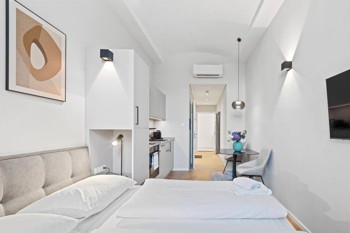 A modern hotel room with a large bed, a desk, and a kitchenette.